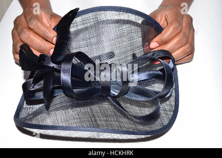 Schwarze weibliche Hände sanft halten ein Marineblau Fascinator auf weißem Hintergrund Stockfoto