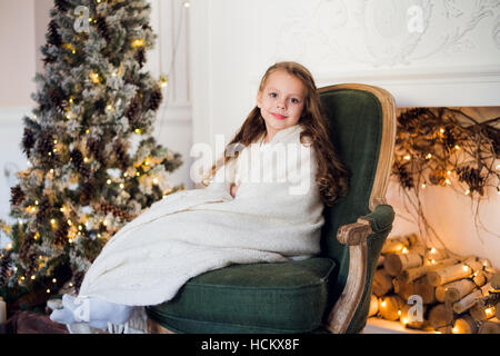 Niedliche kleine Mädchen sitzt durch den Weihnachtsbaum, eingehüllt in eine warme Decke zu Hause Stockfoto