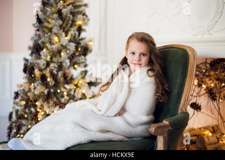 Niedliche kleine Mädchen sitzt durch den Weihnachtsbaum, eingehüllt in eine warme Decke zu Hause Stockfoto