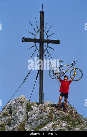 Mann hält ein Mountainbike neben einem Kreuz auf dem Gipfel eines Hügels, Steinerner Jaeger, Reichraming, OÖ, Österreich Stockfoto