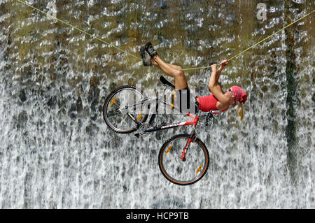 Frau einen Wasserfall an einem Seil mit dem Fahrrad überqueren Stockfoto