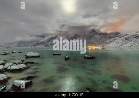 Vollmond leuchtet auf den schneebedeckten Gipfeln spiegelt sich in den kalten See, Vareid, Flakstad, Nordland, Lofoten Inseln, Norwegen Stockfoto