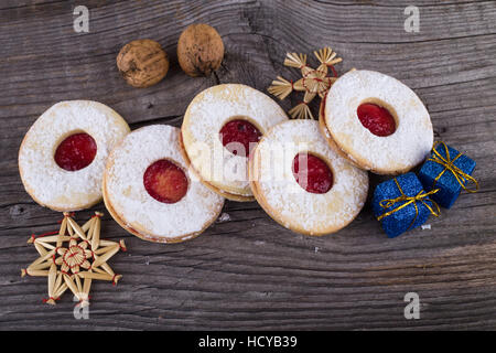 Hausgemachtes Weihnachtsgebäck mit Puderzucker und Marmelade auf alten Holzoberfläche. Weihnachtspakete und Walnüssen. Stockfoto