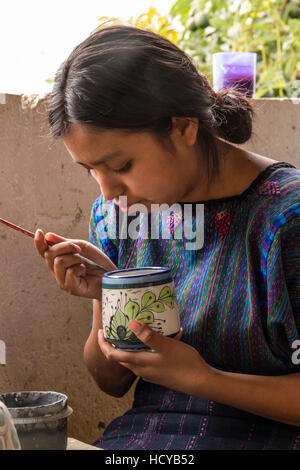 Eine junge Maya-Frau, trägt typische Tracht, malt Designs auf Tonwaren in einer Werkstatt in San Antonio Palopó, Guatemala. Stockfoto