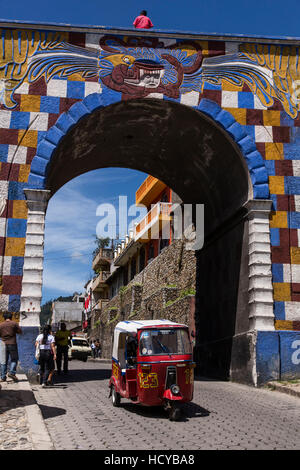 Tuk-Tuks, hergestellt in Indien, sind eine wirtschaftliche Form der öffentlichen Verkehrsmittel in Guatemala.  Durchgang durch das bunte Torbogen Tor in Chichicastenango, Stockfoto