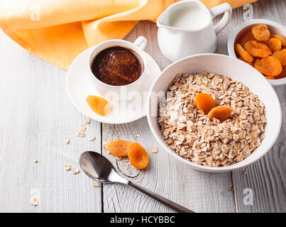Frühstück von Haferflocken mit getrockneten Aprikosen und schwarzen Kaffee auf einem weißen Holztisch Stockfoto