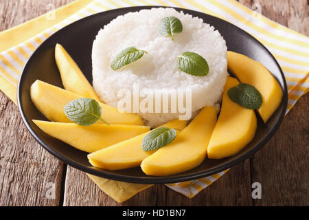 süßer Klebreis mit Kokosmilch und gelbe Mango auf einem Teller auf rustikalen Holztisch Stockfoto