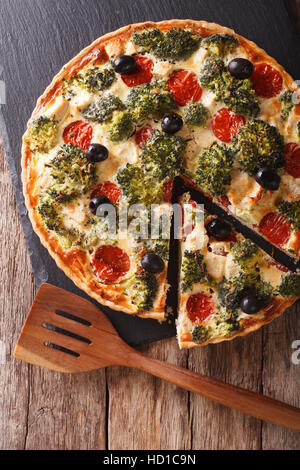 In Scheiben geschnittene Quiche mit Hähnchen, Brokkoli, Tomaten und Oliven Nahaufnahme auf dem Tisch. vertikale Ansicht von oben Stockfoto