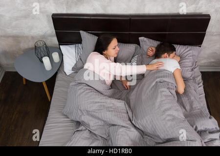 Junge Frau aufwachen ihr beleidigt Freund beim liegen im Bett und Schlafanzug tragen, in der Nähe von Nachttisch mit Kerzen im Schlafzimmer im Loft Stil wi Stockfoto