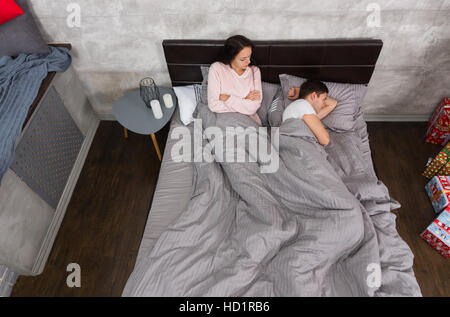 Unglückliche junge Paar geht es nicht nach einem Streit beim liegen im Bett und tragenden Pyjamas, in der Nähe von Nachttisch mit Kerzen im Schlafzimmer im Dachboden Stockfoto