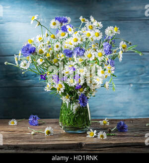 Bouquet von Kamillen und Kornblumen in der Vase auf dem Holztisch. Stockfoto