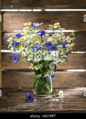 Bouquet von Kamillen und Kornblumen in der Vase auf dem Holztisch. Stockfoto