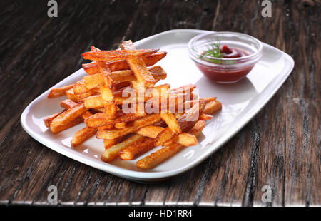 Pommes Frites und Tomaten Sause. Die Platte ist auf dem alten Holztisch. Stockfoto