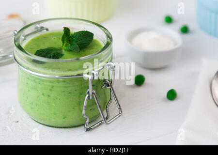 grüne Erbsen Suppe mit Minze im Glas auf weißem Holz Hintergrund Stockfoto