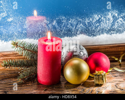 Weihnachtskerze, Weihnachtskugeln und gefrorene Fenster im Hintergrund. Stockfoto