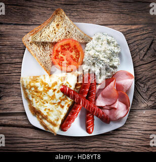 Ein Gericht mit Omelette, Speck und Würstchen auf dem Holztisch. Stockfoto