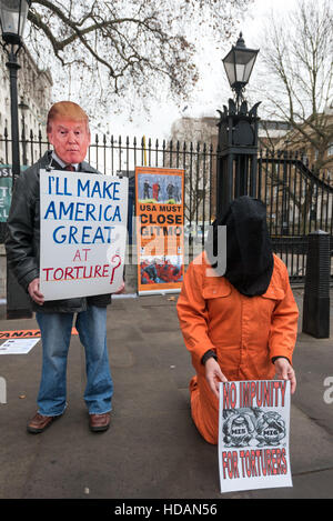 London, UK. 10. Dezember 2016. Ein Mann trägt eine Maske Trump und hält ein Plakat, das liest, "Ich mache große Amerika - Folter?" neben einer knienden Person in einem Sprunganzug Organe und schwarze Kapuze an Guantanamo Gerechtigkeit Kampagne Proteste am Tag der Menschenrechte der Vereinten Nationen gegenüber Downing St fordern ein Ende der Folter, der Schließung von Guantánamo und ein Ende der britischen Mitschuld an Folter. Peter Marshall/Alamy Live-Nachrichten Stockfoto