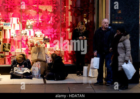 London, UK. 10. Dezember 2016. Weihnachts-Shopping im Londoner West End auf 12.10.2016 in der Oxford Street. Familien sitzen auf dem Bürgersteig, die andere außerhalb eines großen West-End-Speicher warten. Bildnachweis: Julie Edwards/Alamy Live-Nachrichten Stockfoto