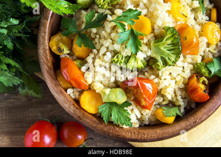 Köstliche hausgemachte vegetarische Bulgur (Couscous) mit Gemüse: Tomaten, Karotten, Zucchini, Brokkoli und Petersilie in rustikalen Holzschale - gesundes Gemüse Stockfoto