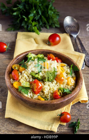 Köstliche hausgemachte vegetarische Bulgur (Couscous) mit Gemüse: Tomaten, Karotten, Zucchini, Brokkoli und Petersilie in rustikalen Holzschale - gesundes Gemüse Stockfoto