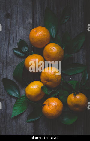 Frische Mandarinen mit grünen Blättern auf rustikalen Holztisch. Ansicht von oben, vertikale Zusammensetzung getönt Bild. Stockfoto