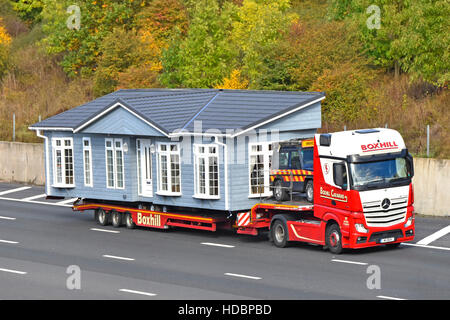 Park Home Lodge ist Teil einer werksseitig montierten, vorgefertigten, breiten Last, die auf einem lkw-Tieflader mit Geländewagen auf der britischen Autobahn transportiert wird Stockfoto