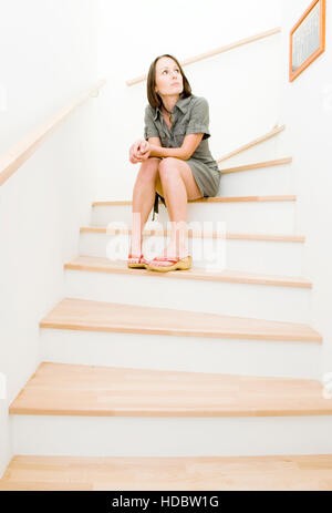 Junge Frau sitzt auf Holztreppen mit Blick auf ein Bild an der Wand Stockfoto