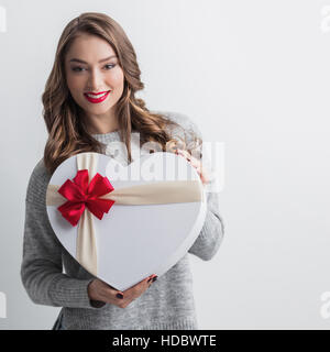 Junges Mädchen mit herzförmigen Geschenkbox auf weißem Hintergrund Stockfoto