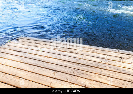 Ecke eine alte hölzerne Pier mit blauen Flusswasser auf einem Hintergrund Stockfoto