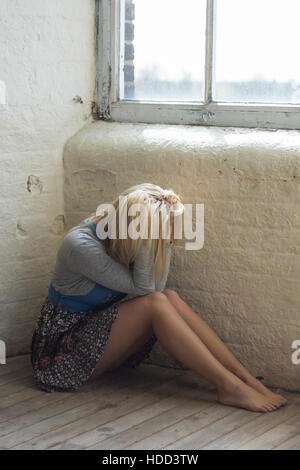 Depressive Frau saß auf dem Boden durch die Fenster Kopf in Händen