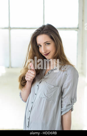 Glückliche junge Frau zeigt ein Daumen hoch Handzeichen im Innenbereich Stockfoto