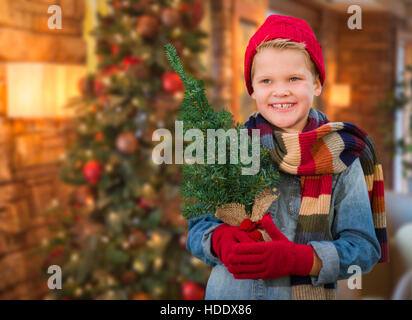 Jungen tragen Handschuhe und Schal In Weihnachten eingerichtetes Zimmer Kleinbaum halten. Stockfoto