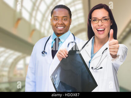 Weiblichen und männlichen kaukasischen und afrikanischen amerikanischen Ärzte im Krankenhaus Büro mit Röntgenfilm und Daumen nach oben. Stockfoto