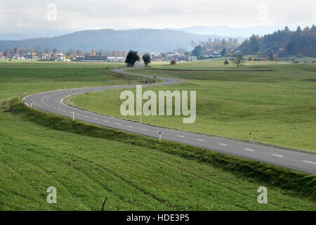 Eine kurvenreiche Straße durch Wiesen und Weiden führt zur Stadt von Logatec, Slowenien Stockfoto