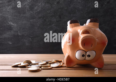 Konzept der Ausgaben der Einsparungen mit Sparschwein kopfüber und Tafel Hintergrund. Horizontale Komposition. Ansicht von vorne. Stockfoto