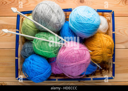 Korb gefüllt mit Kugeln aus Garn und Stricknadeln auf Holzbrettern Stockfoto