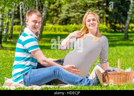 Schöne junge Familie mit einem Picknick im Park, Frau ist schwanger Stockfoto
