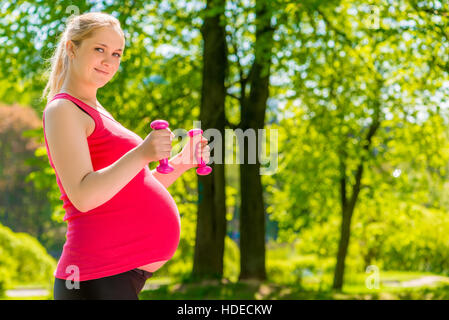 Schwangere Frau Outdoor im Park mit Hanteln Stockfoto