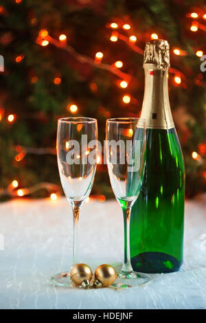 zwei Gläser und eine Flasche Champagner ist auf eine festliche Tischdecke auf dem Tisch vor dem Hintergrund der Weihnachtsbaum und Lichter. Stockfoto