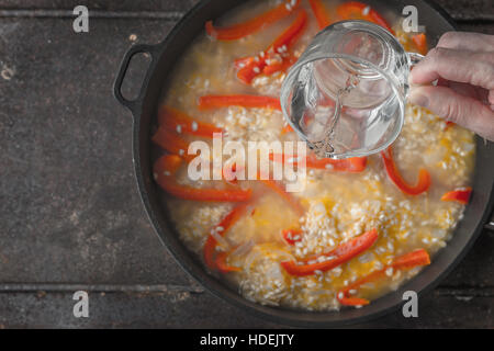 Zugabe von Wasser in der Pfanne mit Reis und Paprika Draufsicht Stockfoto