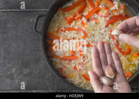 Hinzufügen von Knoblauch in der Pfanne mit Reis und Paprika Draufsicht Stockfoto