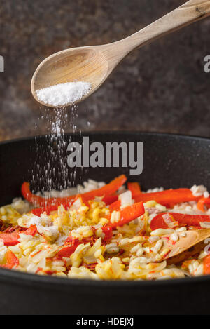 Zugabe von Salz in der Pfanne mit Reis und Paprika vertikale Stockfoto