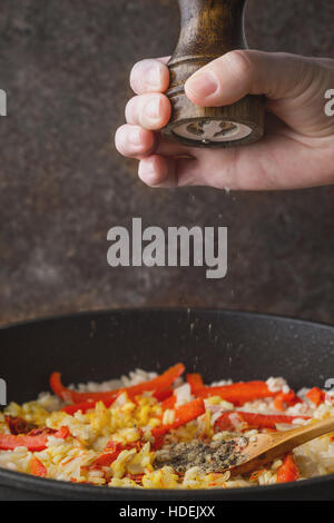 Schwarzer Pfeffer in der Pfanne mit Reis und Paprika vertikale hinzufügen Stockfoto