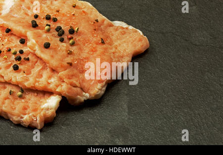 Drei Stücke von rohem Fleisch auf dem Kotelett Schnitzel mit Pfefferkörnern und Salzkristalle auf alten steinernen Küchentisch bestreut. Flache, horizontale Ansicht schließen Stockfoto