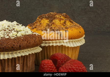 Foto close up zwei Muffins, Schwamm und Kakao bestreut mit geriebener Schokolade und frischen Himbeeren, ein Alter Stein Küchentisch. Horizontale Ansicht von s Stockfoto