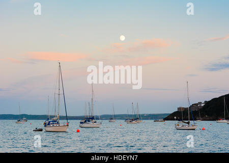 Vollmond über Yachten auf einen ruhigen türkisfarbenen Meer mit roten Zirruswolken verankert. Stockfoto