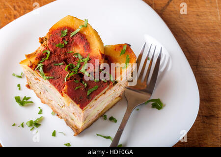 Teil des köstlichen geschichteten Moussaka mit Fleisch und Kartoffeln auf Teller mit Gabel und Petersilie gemacht Stockfoto