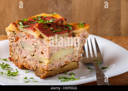 Teil des köstlichen geschichteten Moussaka mit Fleisch und Kartoffeln auf Teller mit Gabel und Petersilie gemacht Stockfoto