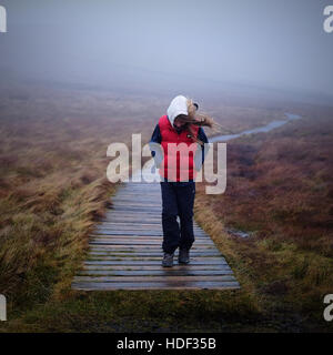 Ein junges Mädchen, gekleidet in warme Kleidung, zu Fuß entlang einer Promenade auf einem Hügel im Winter im Nebel. Stockfoto