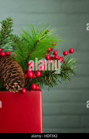 Immergrün, Beeren und Zapfen in einem leuchtend roten Topf. Sehr realistische Dekoration aus linken Seite positioniert. Stockfoto